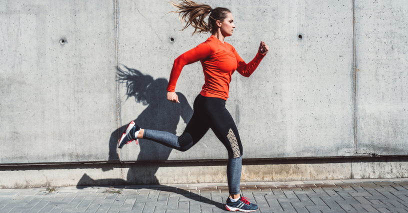 Eine Frau joggt dynamisch an einer Betonwand entlang