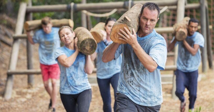 Eine Gruppe von Menschen trägt Baumstämme als Teil eines Outdoor-Fitness-Trainings