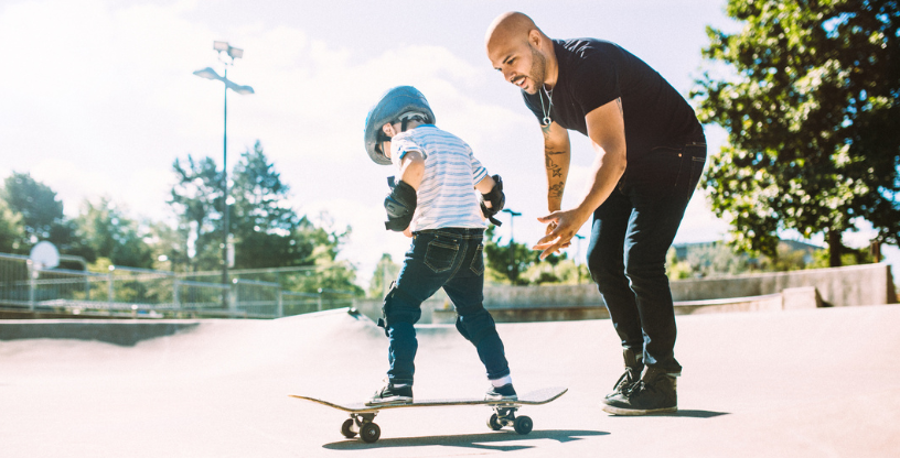 Kind lernt, mit einem Skateboard im Park zu fahren