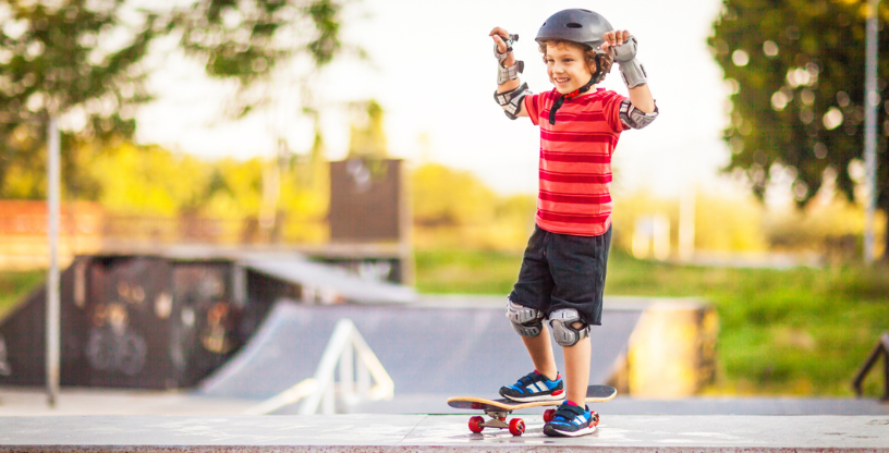 Ein Junge trägt Schutzkleidung und steht auf einem Skateboard im Skatepark